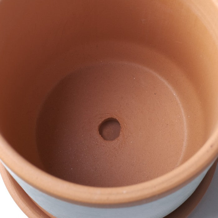 Blick in den Blumentopf „Ino“ mit integriertem Drainageloch im Boden aus rotem Ton und angedeuteter gelber Streifen-Dekoration am oberen Rand.